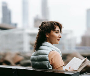 donna-sorridente-che-sta-leggendo-un-libro-all-aria-aperta