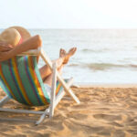 donna-di-spalle-sulla-sdraia-prende-sole-mare-sabbia